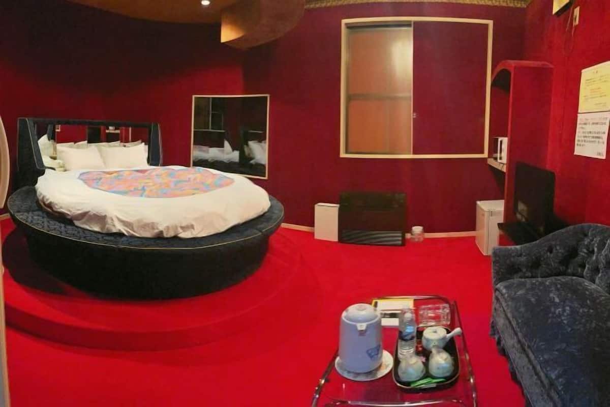 A room with a round bed, a red carpet, a small table with tea and books, and a dark armchair.