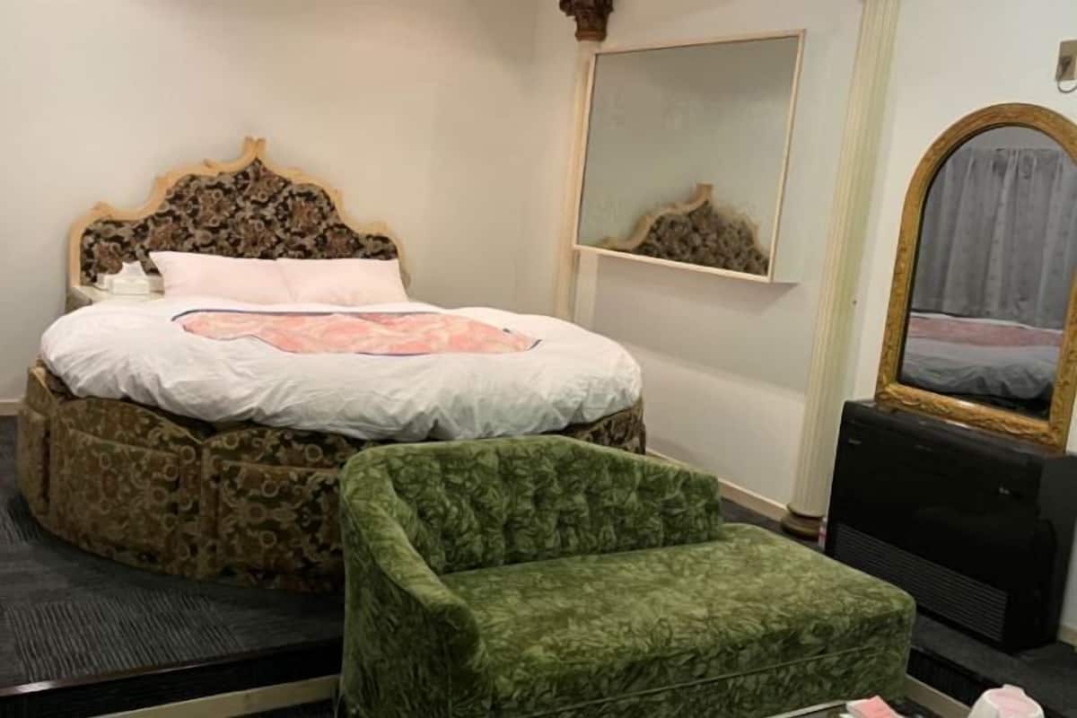 A bedroom with a bed, a green armchair, a mirror, and a heater.