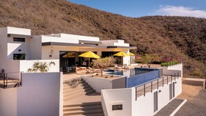 Una casa moderna de dos pisos con piscina, mobiliario exterior y vista a un paisaje montañoso.