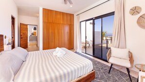 Una habitación de hotel moderna con una cama grande, una puerta corrediza de vidrio a un balcón y un armario de madera.