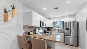 A modern kitchen with white cabinets, stainless steel appliances, and a granite countertop. - 30A Beachside - Steps to Beach! Centrally located, Pools and Tennis! (Santa Rosa Beach)
