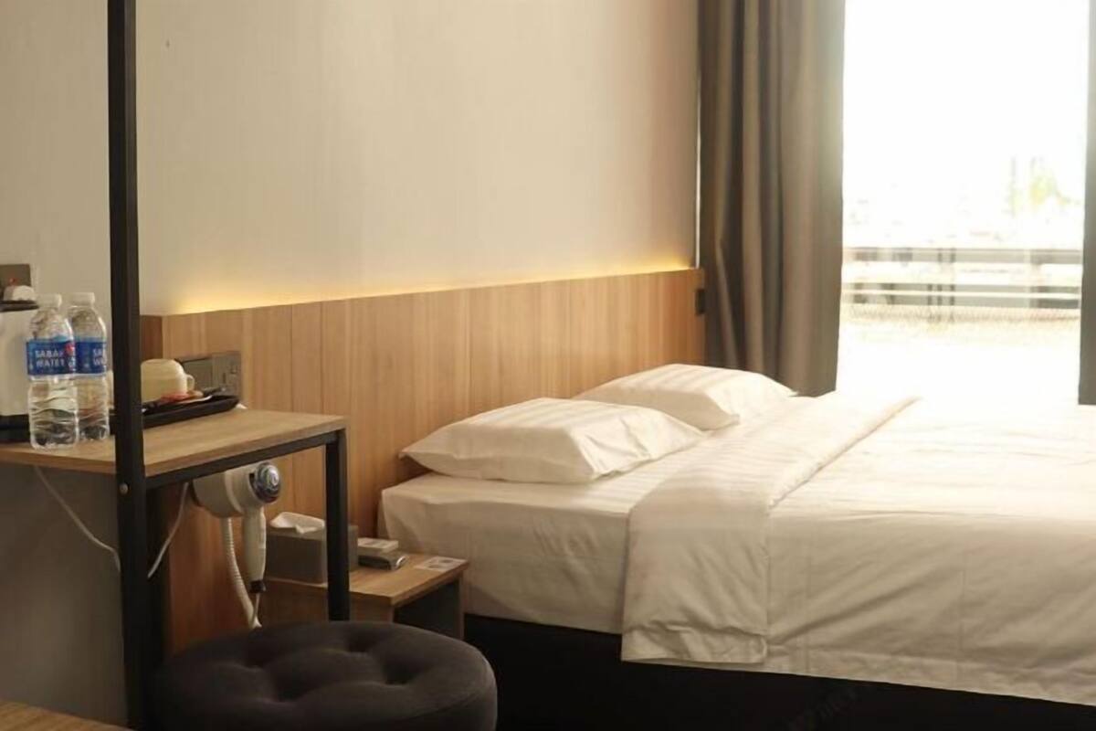 A hotel room with a bed, a desk with a telephone, a chair, and a window with curtains.
