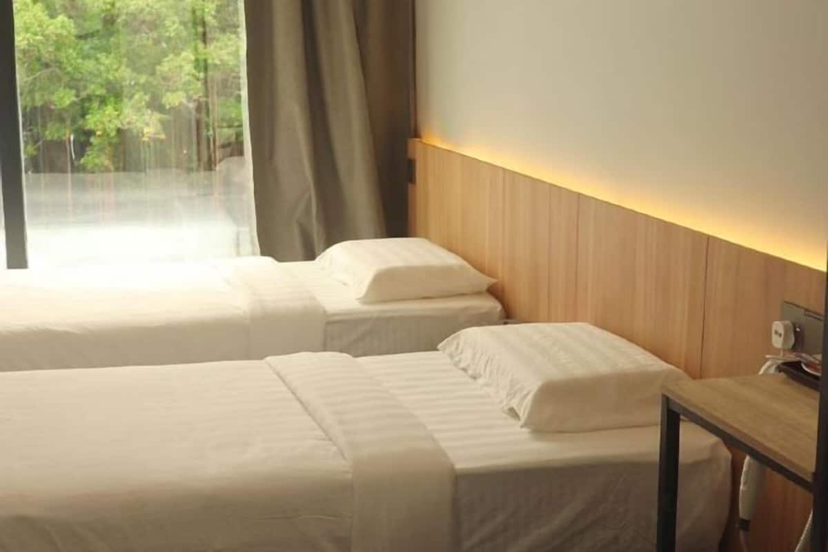 A hotel room with two beds, a wooden headboard, a bedside table, and a window with curtains.