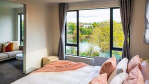 Habitación de hotel con una cama grande, un sofá y vistas a un río y árboles.