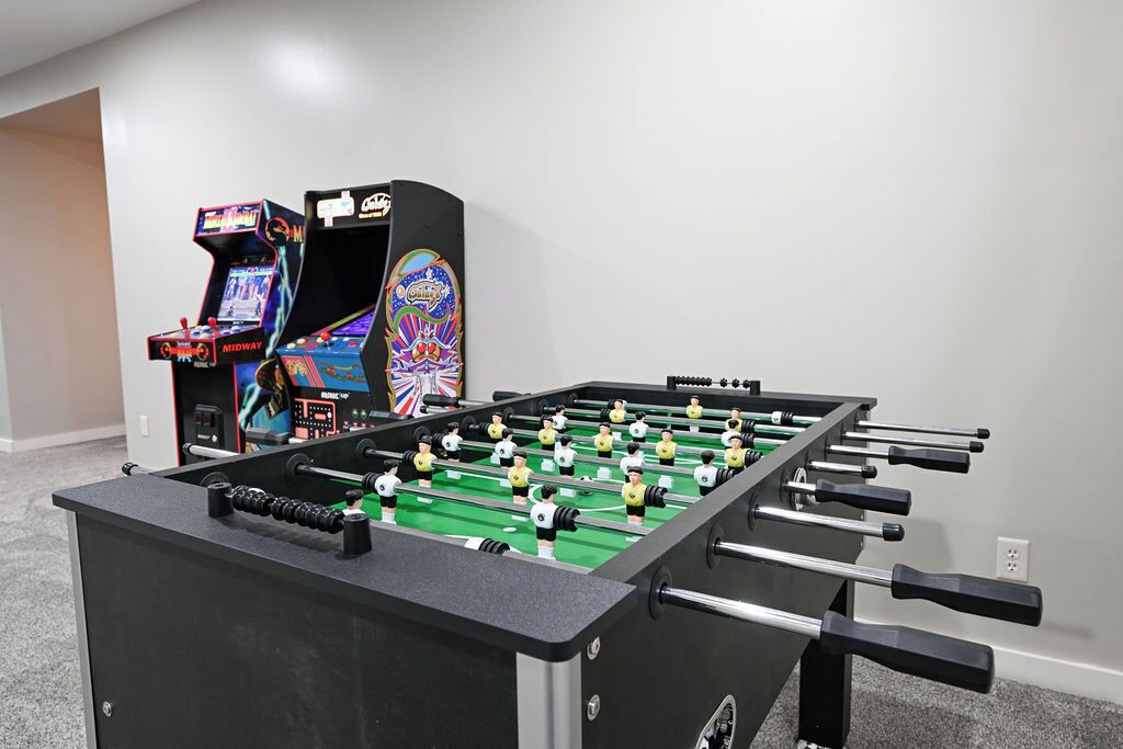 A foosball table with a control panel and a colorful arcade machine in the background.