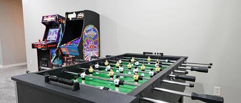 A foosball table with a control panel and a colorful arcade machine in the background.