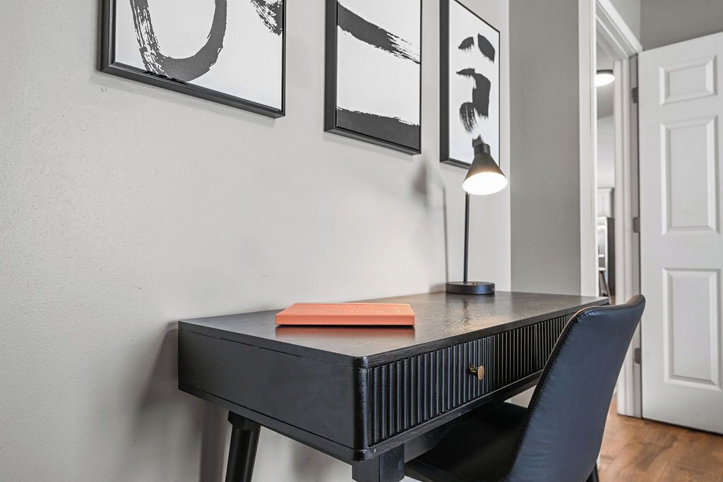 Habitació moderna amb escriptori negre, una cadira i quadres penjats a la paret.