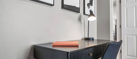 Habitació moderna amb escriptori negre, una cadira i quadres penjats a la paret.