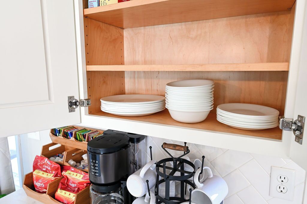 A kitchen with wooden shelves holding white plates and bowls, a coffee maker, and a dish rack.
