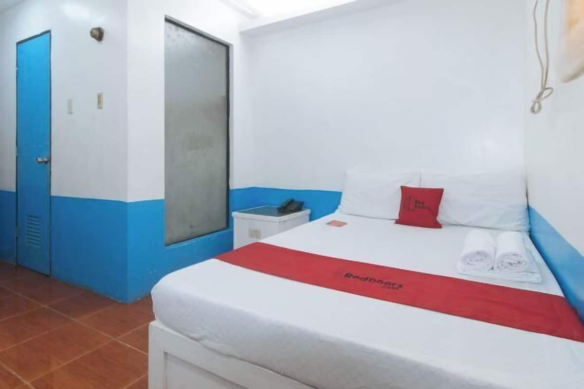 Una habitación de hotel con una cama, un almohadón rojo, un almohadón blanco y una colcha roja y blanca.