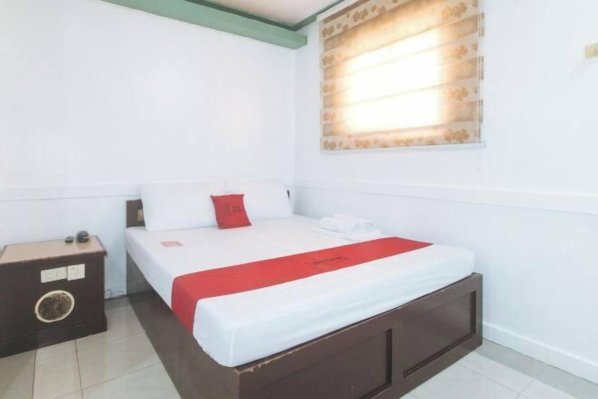 Habitación de hotel con una cama individual, una mesita de noche y una ventana con persianas.