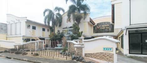 A hotel entrance with a gated driveway, palm trees, and a sign indicating an exit.