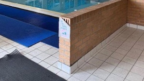Una piscina interna con pavimento piastrellato, parete in mattoni e soffitto con illuminazione incassata.