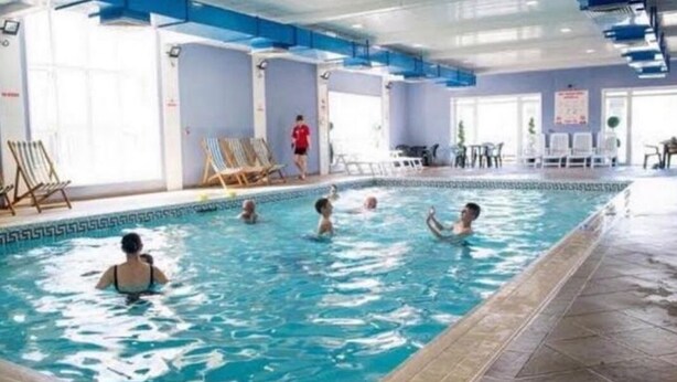 Une piscine intérieure dotée de plusieurs couloirs de nage, de chaises longues et d’une personne qui passe.