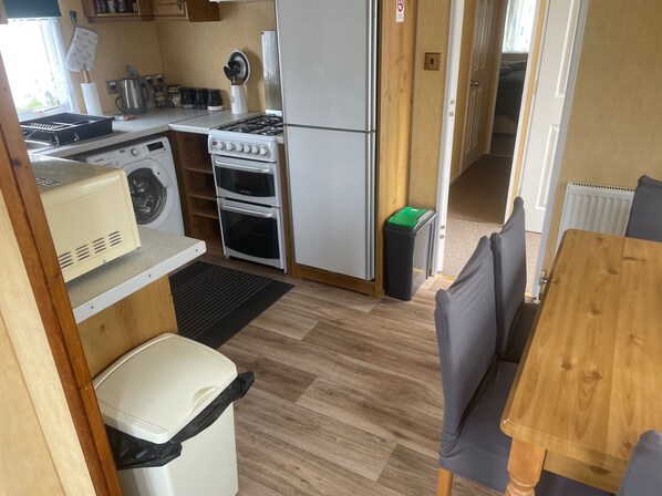 A compact kitchen with a stove, oven, washing machine, and a trash bin.