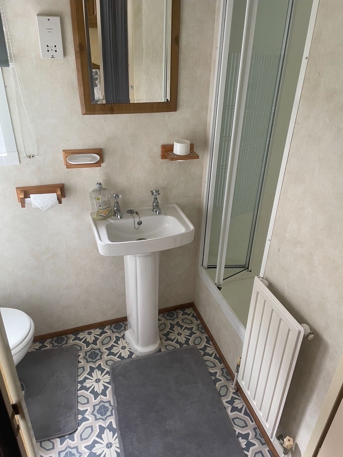 A bathroom with a pedestal sink, a mirror, a towel rack, and a shower area.