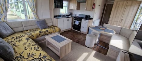 Interior compacto de uma motorhome, com sofá, cozinha pequena e área de refeições.
