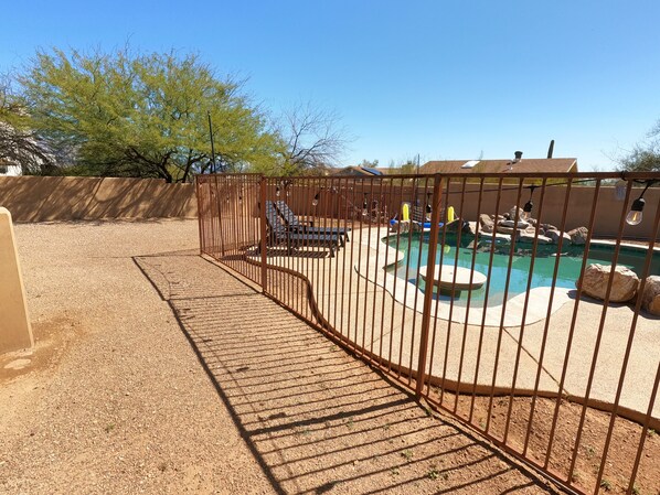 Un área exterior cercada con piscina, tobogán y una formación rocosa.