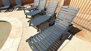 Sillones de exterior dispuestos en filas, con una cerca metálica y una zona pavimentada al fondo.