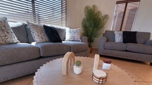 Una sala de estar con dos sofás grises, una mesa de centro redonda de madera con adornos, y una planta grande en maceta.