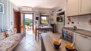 Un espace de vie compact comprenant un canapé, une table à manger, un coin cuisine et une vue sur la verdure environnante.