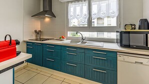 A modern kitchen with teal cabinets, a black microwave, and a red kettle. - Apartment Le Zal by Interhome (Quiberon)