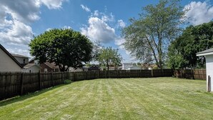 Un patio trasero con cerca de madera, un árbol grande y casas al fondo.