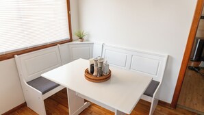 Una mesa blanca con una cesta tejida, ubicada en un rincón junto a un banco.