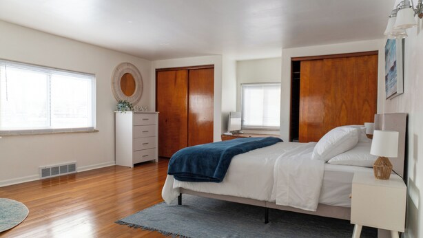 Un dormitorio con cama, mesita de noche, cómoda y un gran ventanal.
