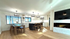 Une cuisine moderne avec un coin repas, un plancher en bois, des luminaires suspendus et une cheminée.