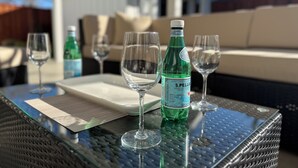 Une table en verre avec une bouteille d’eau pétillante S. Pellegrino, deux verres à vin et une assiette blanche.