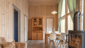 A cozy cabin interior with a wooden dining table, white chairs, a sofa with patterned cushions, a kitchen area with cabinets, and a wood-burning stove. - Ferienhaus mit Sauna im Ferienpark Mirow (Mirow)