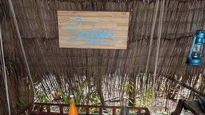 A table set for breakfast with various dishes, a wooden sign above, and a thatched roof background. - swims maldives (Omadhoo)