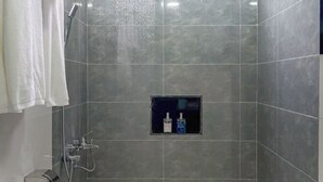 A shower area with grey tiles, a small shelf with toiletries, and a white towel rack. - swims maldives (Omadhoo)