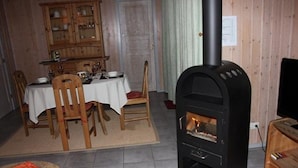 A dining area with a table set for four, a black wood-burning stove, and a wooden cabinet in the background. - Ferienhaus mit Sauna im Ferienpark Mirow (Mirow)