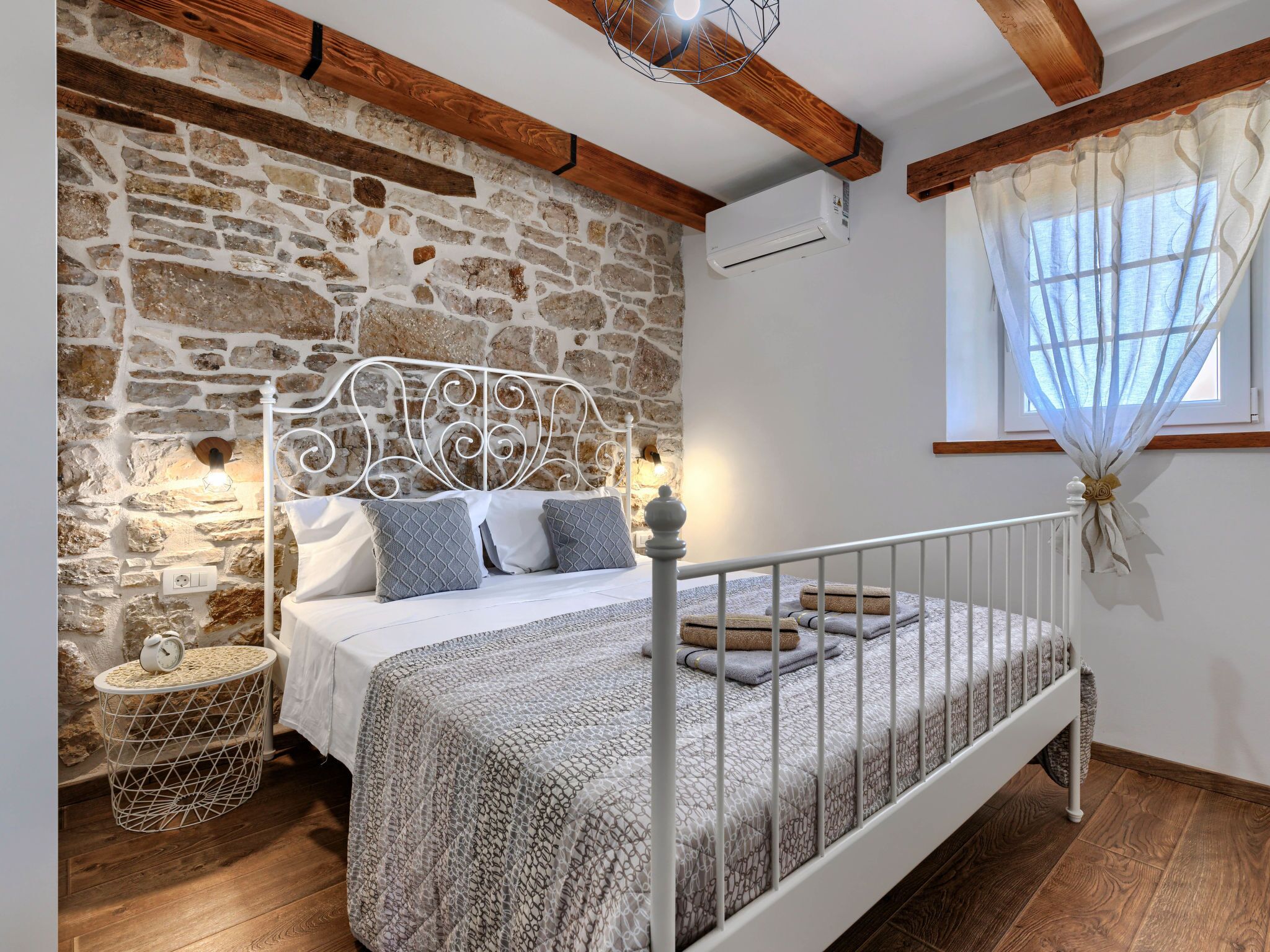 Ein Schlafzimmer mit einer Steinsäule, einem weißen Metallbettgestell und einer Holzbalkendecke.
