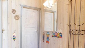 Un couloir avec une porte blanche, un miroir et un présentoir métallique muni de crochets.