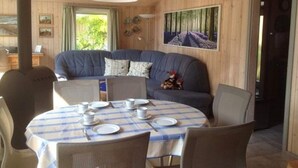 Une pièce chaleureuse avec une table ronde pour quatre personnes, un canapé bleu et une grande fenêtre donnant sur les arbres.