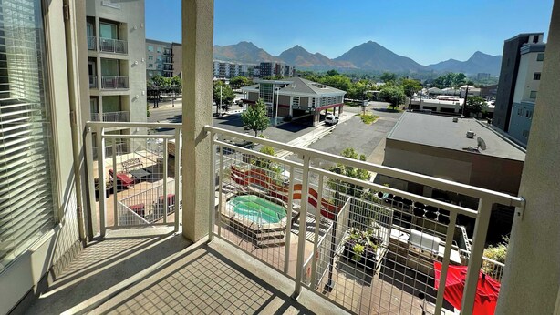 Un balcón con vistas a una piscina, una gasolinera y montañas al fondo.