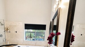 A modern bathroom with a bathtub, a large mirror, and a window.