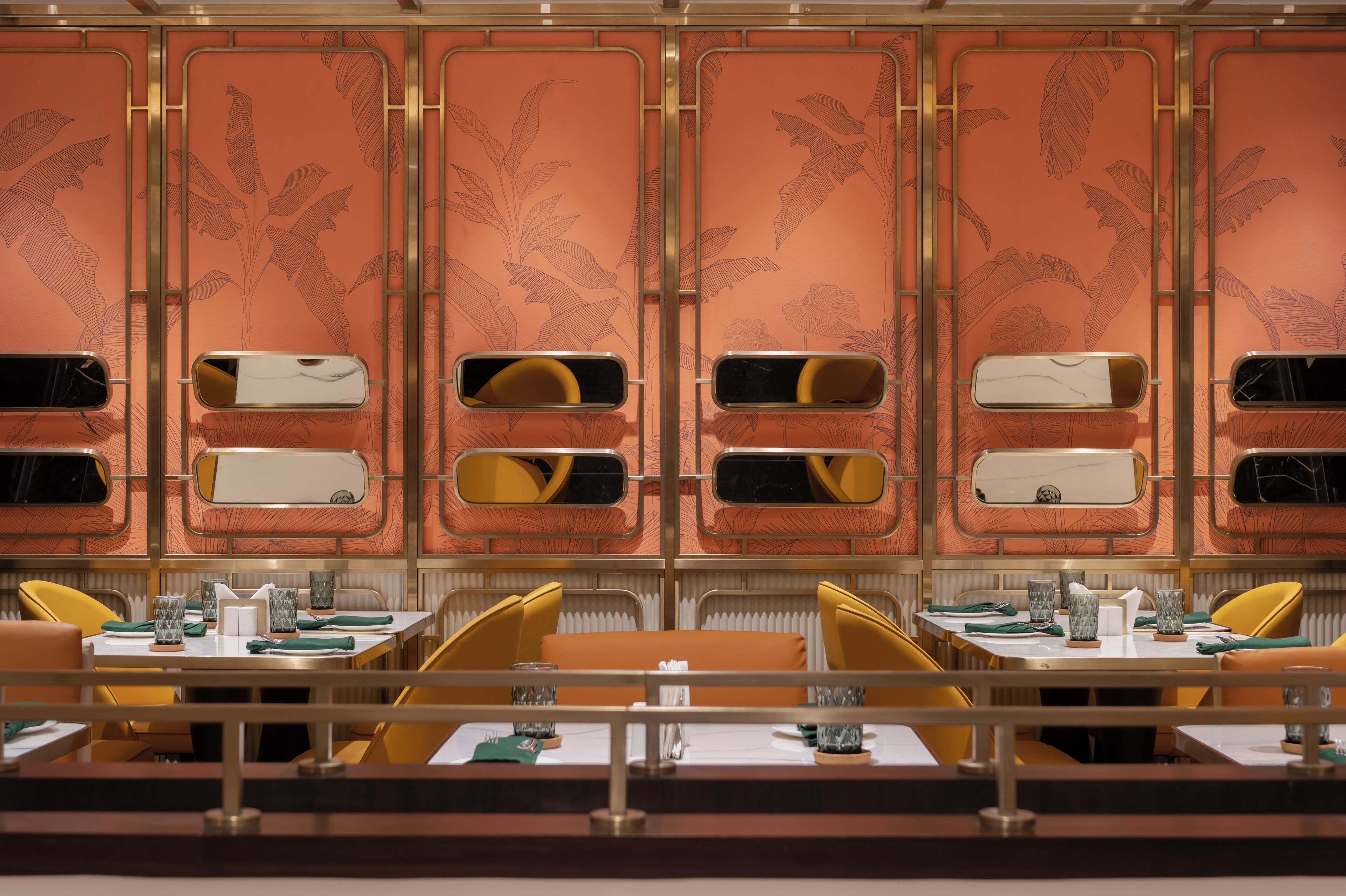 A restaurant with a tropical leaf pattern on the walls, yellow chairs, and tables set with white tablecloths and green napkins.