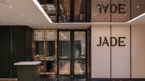 A modern interior with a glass door entrance, a visible dining area with tables and chairs, and the word "JADE" on the wall. - The Magnus Hotel (Coimbatore)
