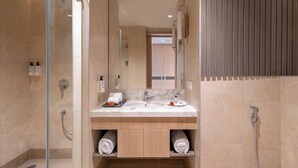 A modern bathroom with a glass-enclosed shower, a marble sink, wooden cabinets, and a mirror. - The Magnus Hotel (Coimbatore)