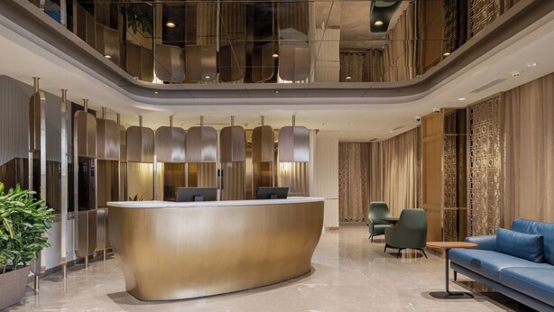 A modern reception area with a curved counter, seating, and a decorative plant. - The Magnus Hotel (Coimbatore)