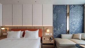 A hotel room with a bed, a sofa, a nightstand with a phone, and a wall with a decorative pattern. - The Magnus Hotel (Coimbatore)