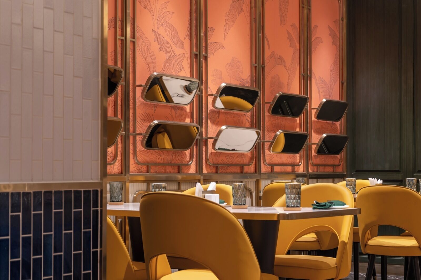 L’intérieur d’un restaurant avec des chaises jaunes, un mur recouvert de carreaux et un papier peint à motifs.