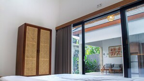 Une chambre à coucher comprenant un lit, une armoire et une porte-fenêtre coulissante donnant sur un balcon équipé d’une chaise et de plantes.