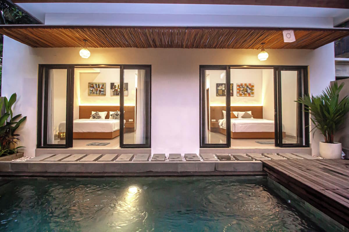 A modern hotel with two bedrooms, each with a large window, a wooden ceiling, and a small pool area.