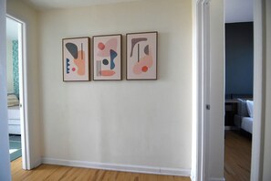 A hallway with three abstract paintings on the wall, wooden flooring, and a door leading to another room.