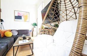 A modern living room with a sofa, a coffee table, a white armchair, a wicker chair, and a bookshelf. - Seaside Sanctuary - Rooftop Deck & Hot Tub (Hermosa Beach)